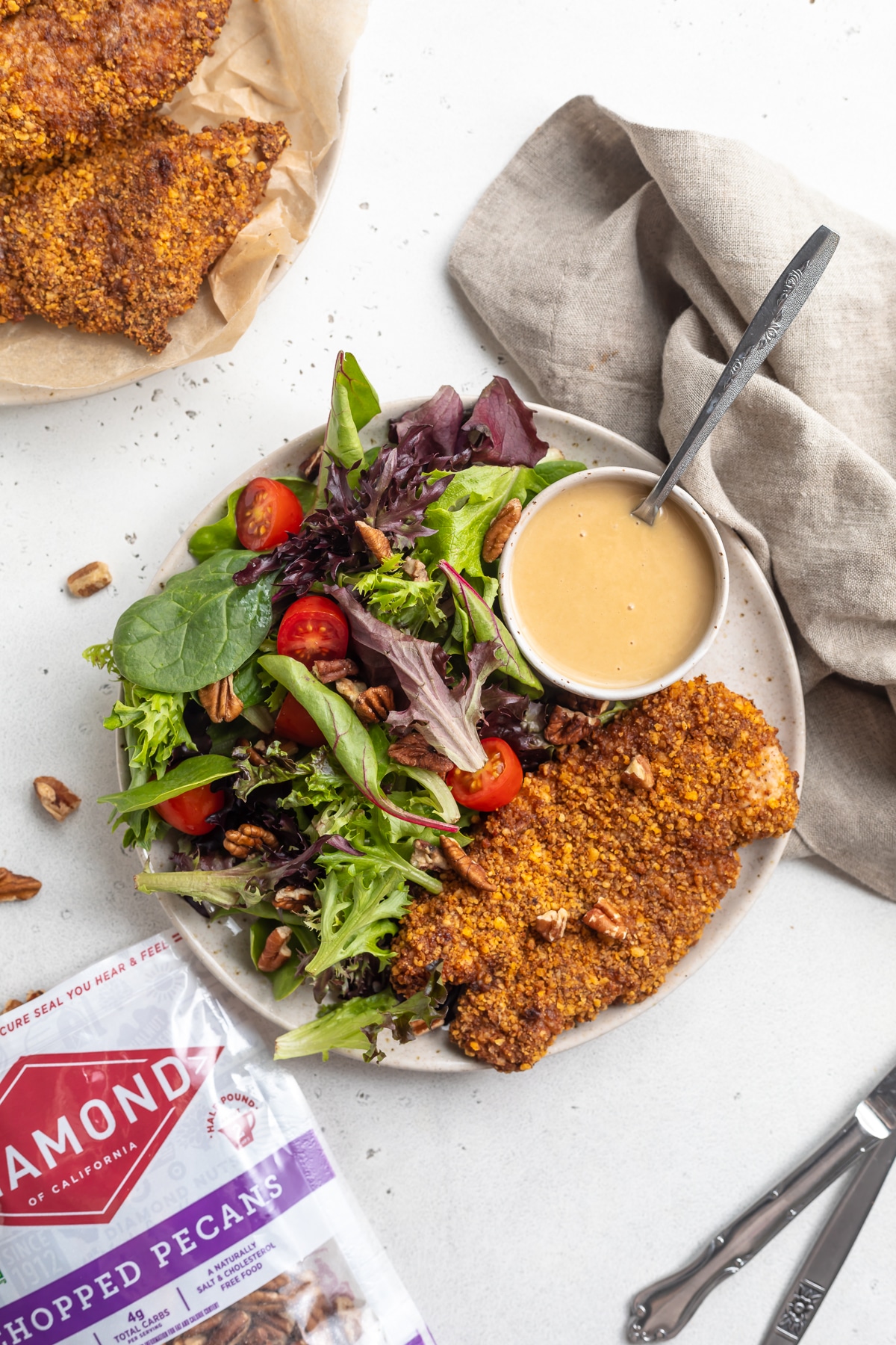 Plate with air fryer pecan crusted chicken and large salad, next to bag of Diamond chopped pecans.