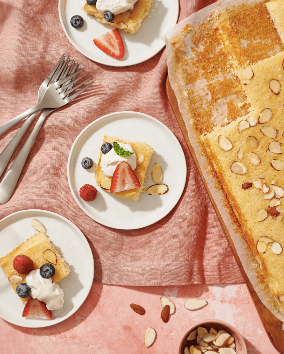 Slices of Honey Nut Sheet Cake with Berries and Cream on pink tablecloth.