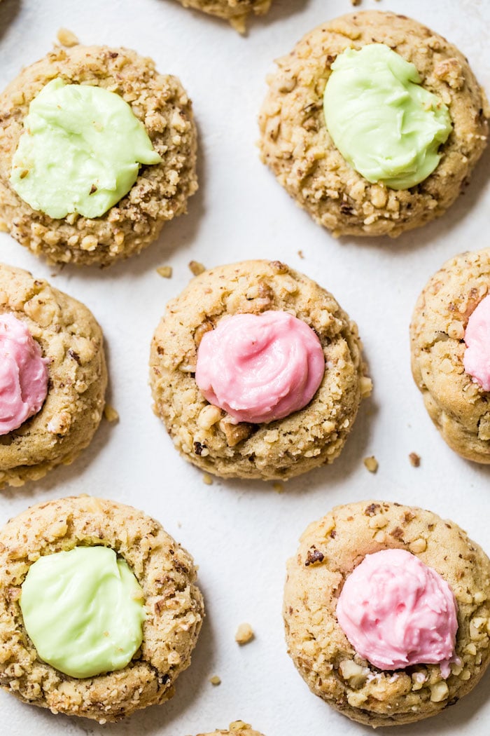 Buttercream Walnut Thumbprint Cookies, half with green frosting, half pink.
