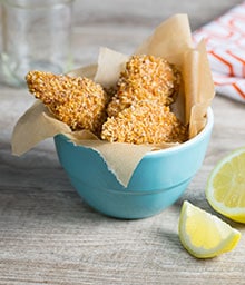 Bowl of three Crispy Pecan Chicken Tenders next to sliced lemon.