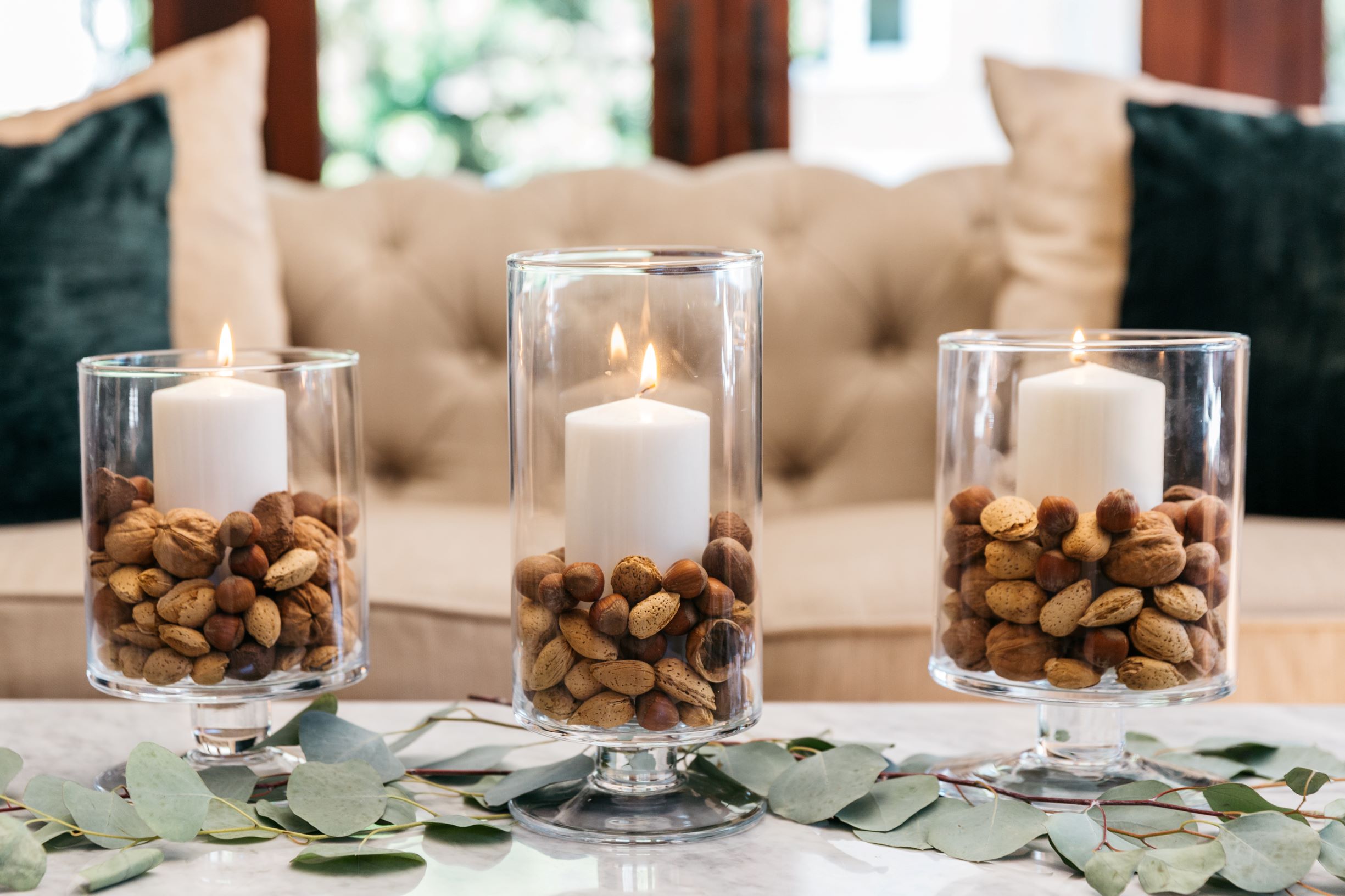 Three DIY votive candle holders surrounded by leaves on a table.