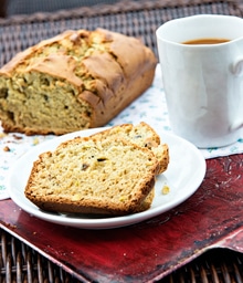 Loaf and slices of Pistachio Quickbread next to cup of coffee.