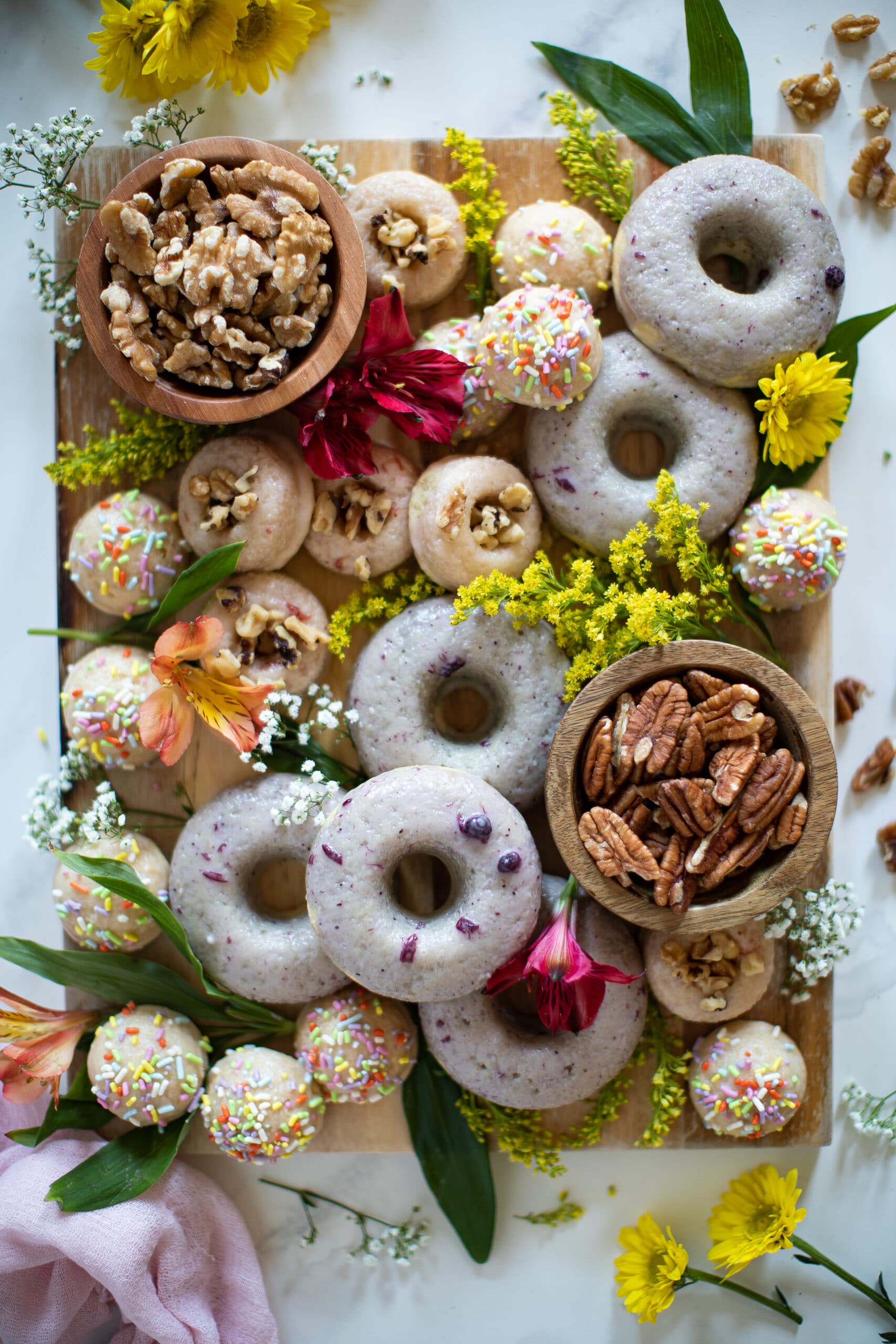 Dessert board featuring Vegan Vanilla Pecan Donuts, other treats, flowers, and nuts.