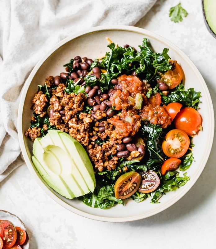 Plate of Kale Taco Salad with sliced avocado and cherry tomatoes.