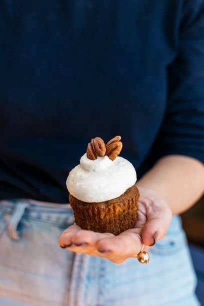 Person holding a Pecan and Walnut Carrot Cake Cupcake with Buttercream Cheese Frosting.