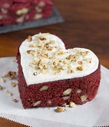 Heart-shaped Red Velvet Brownie with white frosting and chopped nuts.