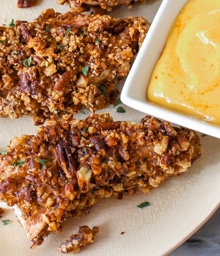 Two pieces of Sallys Baking Pecan Crusted Chicken and dipping sauce.