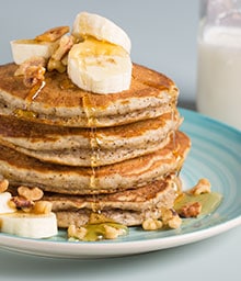 Stack of Walnut Buttermilk Pancakes topped with bananas, walnuts, and syrup.