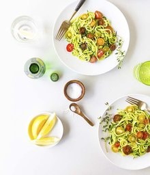 Two plates of Noodled Zucchini with Pistachio Pesto and cherry tomatoes.