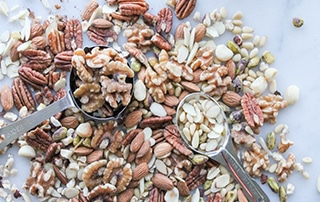 Mixed nuts on a countertop with measuring spoon and cup.