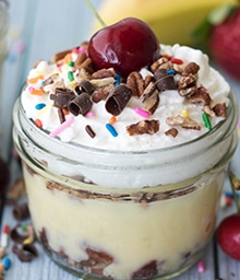 Jar of Banana Split Pudding with cherry and sprinkles on top.