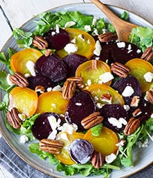 Salad topped with sliced red and golden beets, pecans, and goat cheese.