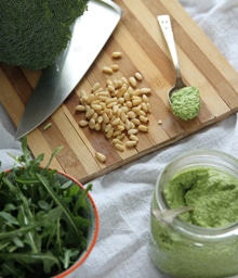 Jar of Broccoli Arugula Pesto and ingredients on a counter.