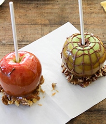 Person piping spider web design on caramel apples.
