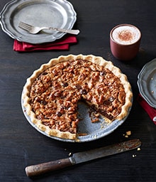 Chocolate Walnut Pie with one slice taken out next to a cappuccino.