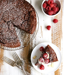 Slice taken out of Flourless Chocolate Almond Cake topped with raspberries.