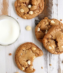 Toffee White Chocolate Macadamia Nut Cookies with a bite taken out and glass of milk.