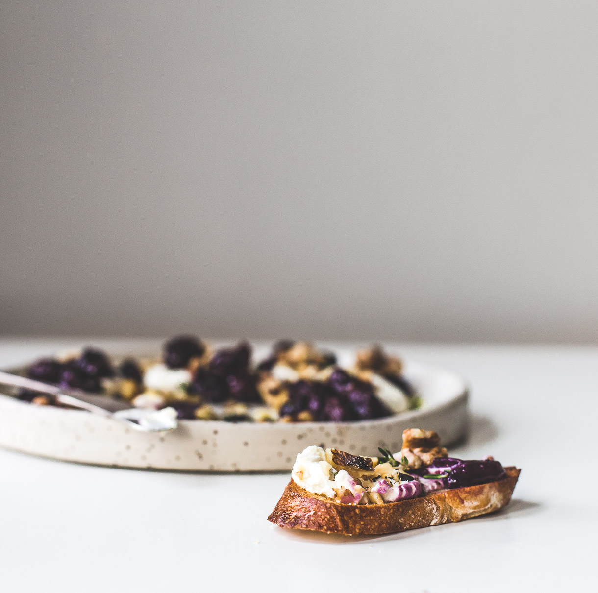 Piece of bread topped with Marinated Goat Cheese with Roasted Grapes and Walnuts.