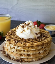Stack of Honey Pecan Waffles topped with whipped cream.