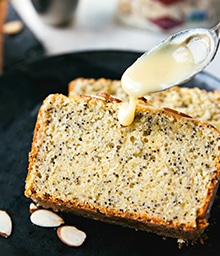 Spoon drizzling topping on Healthy Greek Yogurt Lemon Poppyseed Bread.