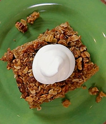 Square of Oatmeal Cake with Cinnamon Pecan Crumble topped with whipped cream.