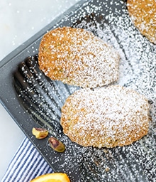 Orange Pistachio Madeleines covered in powdered sugar.