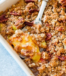 Spoon scooping Peach Pecan Crisp from casserole dish.