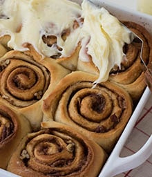 Person putting frosting on Brown Butter Pecan Cinnamon Rolls.