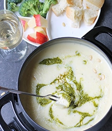 Person dipping bread cube into pot of Pesto Cheese Fondue.