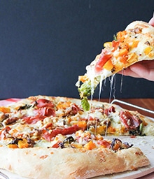 Person grabbing cheesy piece of Winter Vegetable Pizza with Walnuts.