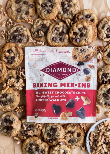 Bag of Diamond Nuts Baking Mix-Ins surrounded by dozens of Chocolate Chip Walnut Cookies.