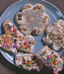 Plate of Frosted Sugar Cookies of different shapes decorated with nuts and sprinkles.