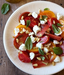 Plate of tomato salad with cheese, herbs, and pine nuts.